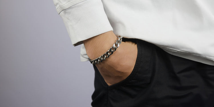 Mann mit Hand in Hosentasche trägt silbernes Panzerarmband in lässigem schwarz-weißen Outfit